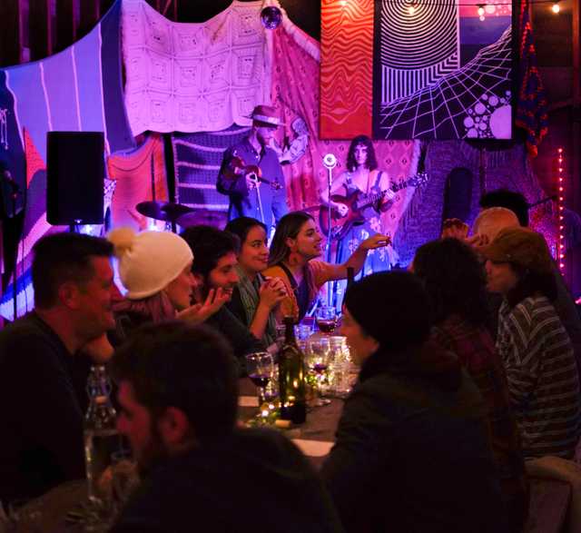 People gathered around a dinner table while listening to a live performance