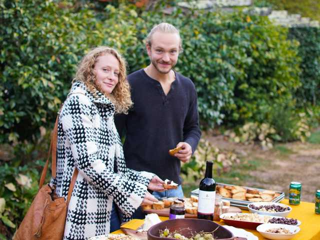 A woman and a man sampling bread and cheese.