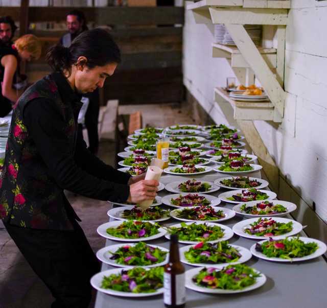 A cook plating a line of dishes to be served.